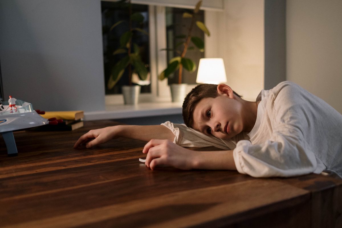 Child resting listlessly on a table at home, showing low mood and withdrawal