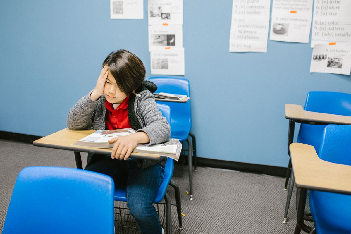 Worried child sitting alone at a classroom desk, head resting on one hand